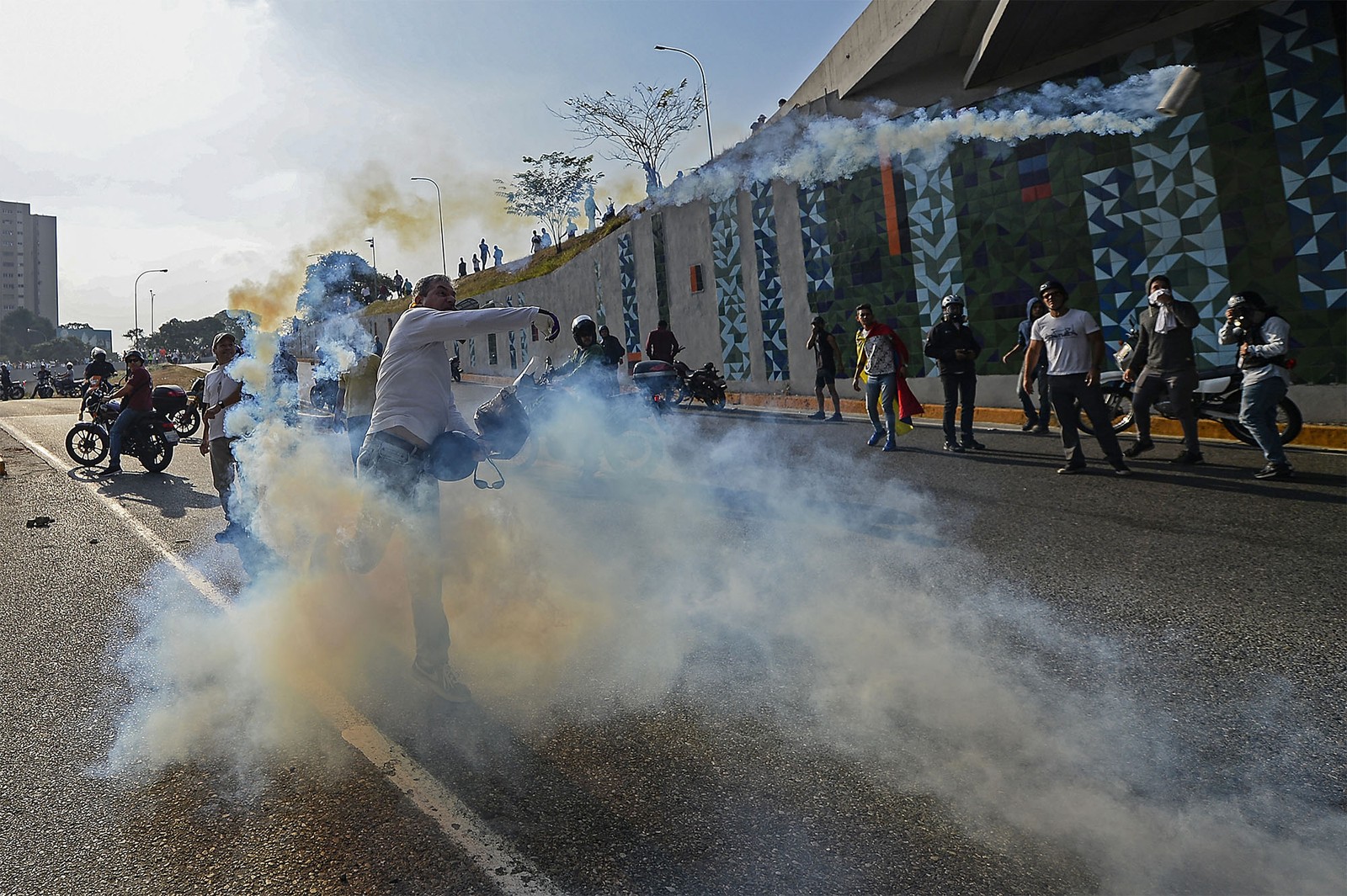 Manifestante apoiador de Guaidó atira de volta uma bomba de gás-lacrimogêneo atirada por forças de Maduro
