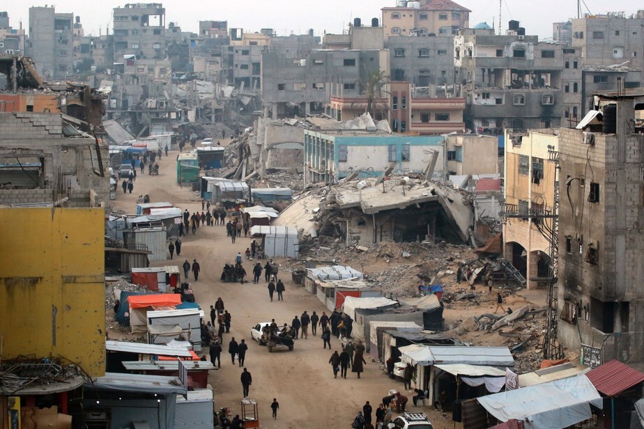 Pessoas passam por barracas que vendem produtos em meio aos escombros de edifícios destruídos durante ataques israelenses