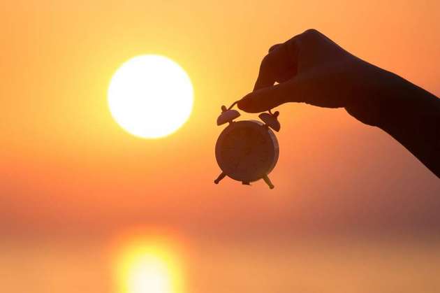 Um homem segurando um relógio de cabeceira diante do sol