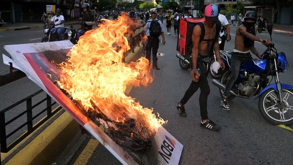 Manifestantes queimam banner durante protesto em Caracas um dia após a eleição presidencial na Venezuela